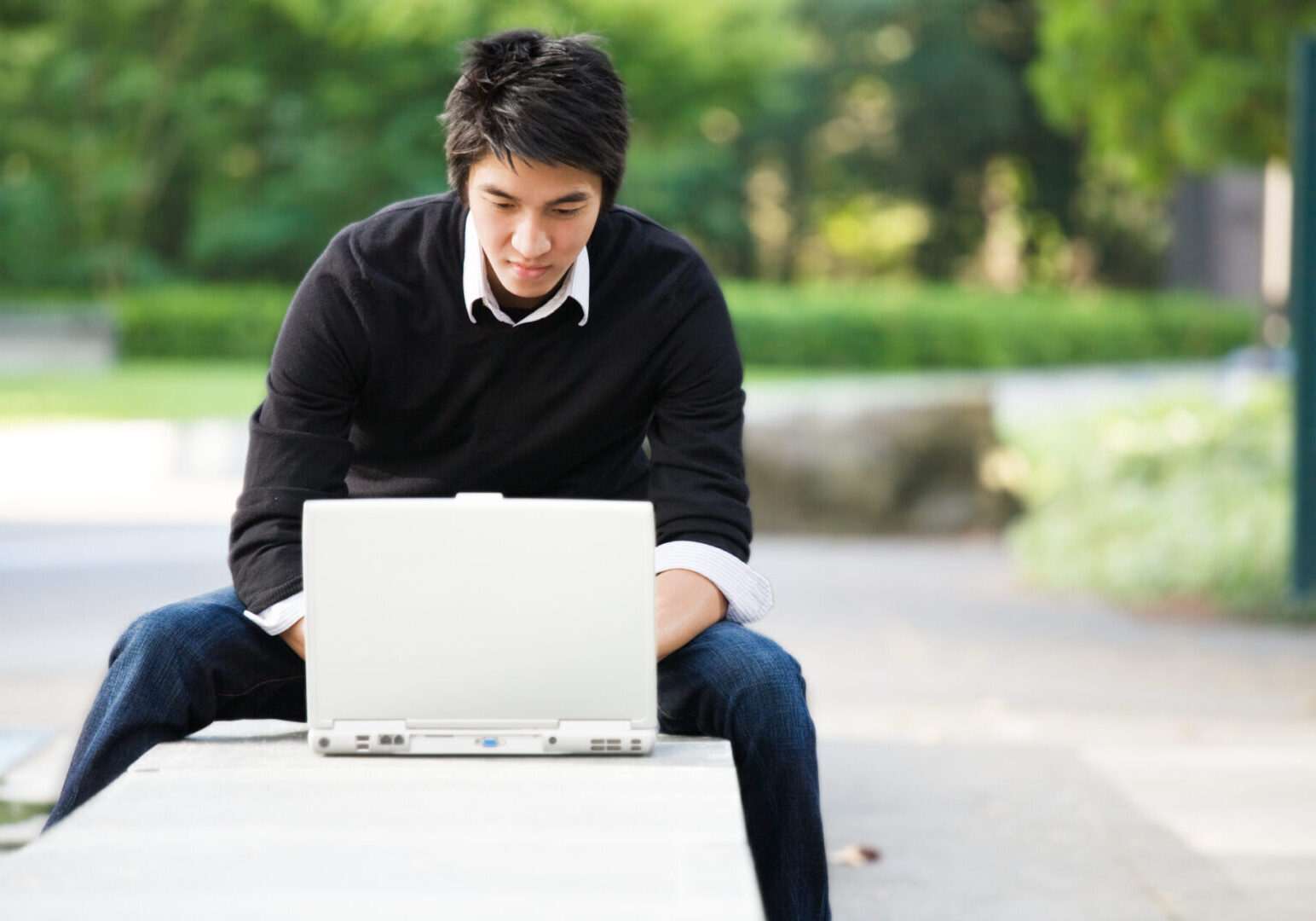 A shot of an asian student working on his laptop at the campus